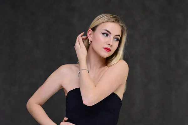 Begreppet modern glamour, kosmetika och skönhet med en söt flicka. Porträtt av en fashionabel vacker blond modell med långt hår, bra makeup, på en grå bakgrund. — Stockfoto