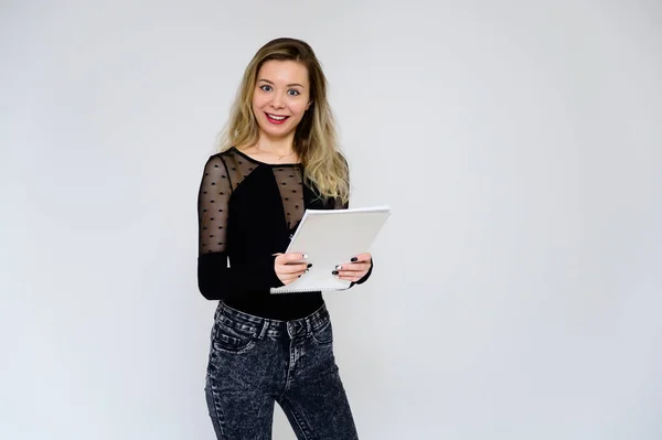 Concepto de una mujer hablando con la cámara. Una foto de una chica muy sonriente con el pelo rizado en una camiseta negra sobre un fondo blanco está de pie justo en frente de la cámara con una carpeta en las manos . — Foto de Stock