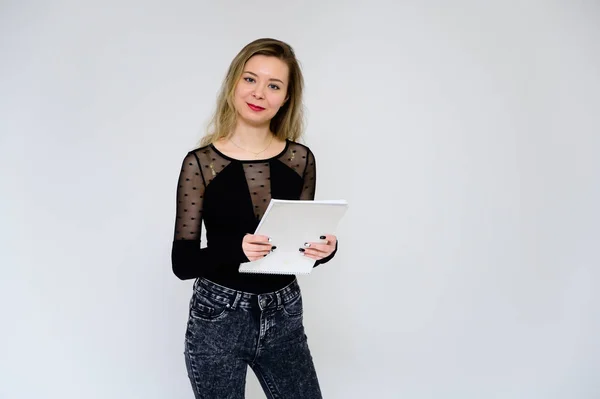 Concepto de una mujer hablando con la cámara. Una foto de una chica muy sonriente con el pelo rizado en una camiseta negra sobre un fondo blanco está de pie justo en frente de la cámara con una carpeta en las manos . — Foto de Stock