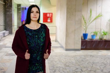 Bir binanın lobisindeki bir modelin göz kamaştırıcı fotoğrafı. Girişteki kamu binasının içinde bordo paltolu güzel esmer bir kadının portresi..