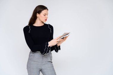 Beyaz bir arka planda elinde beyaz bir klasörle yetişkin bir kız hayal et. Gri pantolonlu, siyah kazaklı güzel bir esmer kızın fotoğrafı gülümsüyor ve farklı pozlarda farklı duygular gösteriyor..