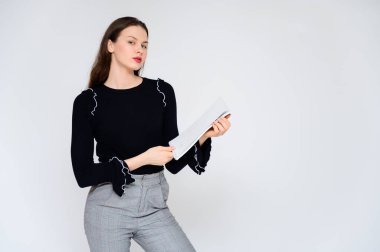 Beyaz bir arka planda elinde beyaz bir klasörle yetişkin bir kız hayal et. Gri pantolonlu, siyah kazaklı güzel bir esmer kızın fotoğrafı gülümsüyor ve farklı pozlarda farklı duygular gösteriyor..