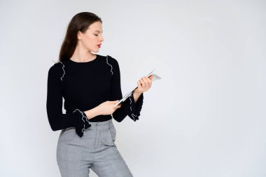 Beyaz bir arka planda elinde beyaz bir klasörle yetişkin bir kız hayal et. Gri pantolonlu, siyah kazaklı güzel bir esmer kızın fotoğrafı gülümsüyor ve farklı pozlarda farklı duygular gösteriyor..