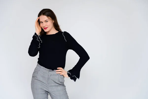 Concept adult girl on a white background. A photo of a pretty brunette girl in gray trousers and a black sweater smiles and shows different emotions in different poses right in front of the camera. — Stock Photo, Image