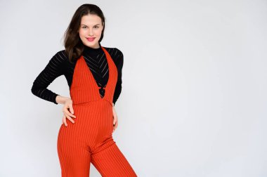 Beyaz arka planda yetişkin bir kız. Kırmızı pantolonlu ve siyah kazaklı güzel bir esmer kızın fotoğrafı gülümsüyor ve kameranın önünde farklı pozlarda farklı duygular gösteriyor..