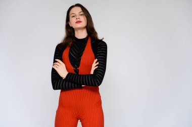 Beyaz arka planda yetişkin bir kız. Kırmızı pantolonlu ve siyah kazaklı güzel bir esmer kızın fotoğrafı gülümsüyor ve kameranın önünde farklı pozlarda farklı duygular gösteriyor..