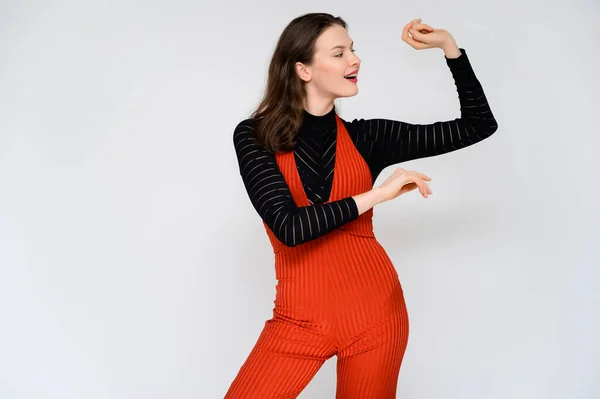 Conceito menina adulta em um fundo branco. Uma foto de uma linda garota morena de calças vermelhas e uma camisola preta sorri e mostra emoções diferentes em poses diferentes bem na frente da câmera . — Fotografia de Stock