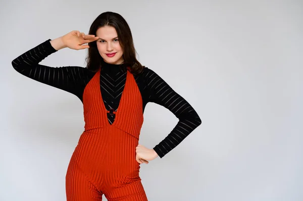 Conceito menina adulta em um fundo branco. Uma foto de uma linda garota morena de calças vermelhas e uma camisola preta sorri e mostra emoções diferentes em poses diferentes bem na frente da câmera . — Fotografia de Stock