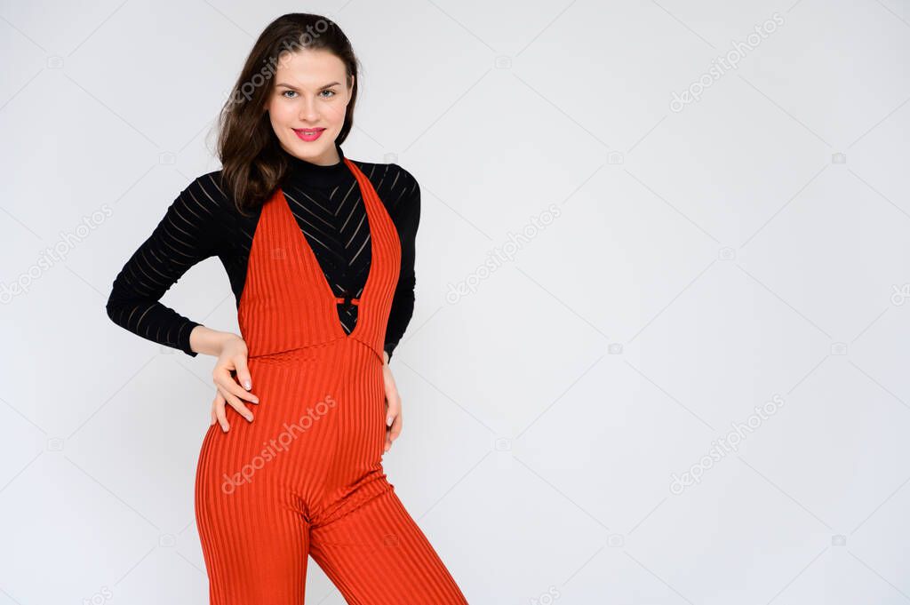 Concept adult girl on a white background. A photo of a pretty brunette girl in red trousers and a black sweater smiles and shows different emotions in different poses right in front of the camera.