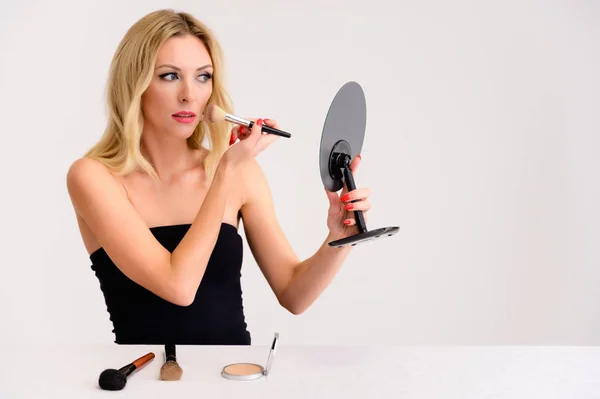 Skönhet och kosmetika koncept. Porträtt av en söt blond modell kvinna med utmärkt makeup, vackert hår och ren hud på en vit bakgrund är att tillämpa makeup med en spegel i händerna. — Stockfoto
