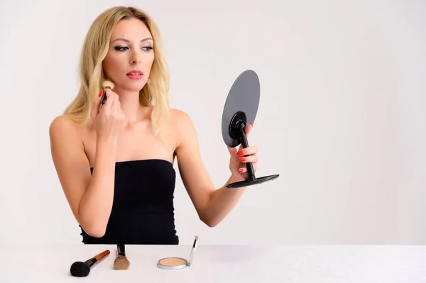 Skönhet och kosmetika koncept. Porträtt av en söt blond modell kvinna med utmärkt makeup, vackert hår och ren hud på en vit bakgrund är att tillämpa makeup med en spegel i händerna. — Stockfoto