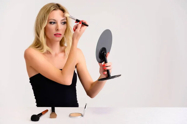 Skönhet och kosmetika koncept. Porträtt av en söt blond modell kvinna med utmärkt makeup, vackert hår och ren hud på en vit bakgrund är att tillämpa makeup med en spegel i händerna. — Stockfoto