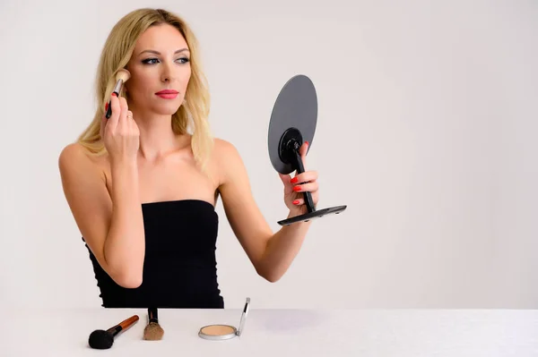 Skönhet och kosmetika koncept. Porträtt av en söt blond modell kvinna med utmärkt makeup, vackert hår och ren hud på en vit bakgrund är att tillämpa makeup med en spegel i händerna. — Stockfoto