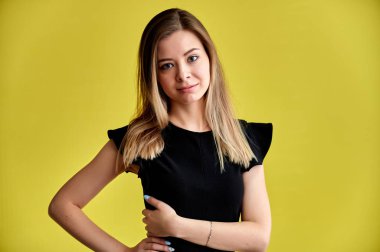 Sarı arka planda, uzun düz saçlı, siyah elbiseli, gülümseyen güzel bir kadının yakın plan portresi. Kameranın önünde durmak, duygularını gösterir, farklı pozlarda konuşur..