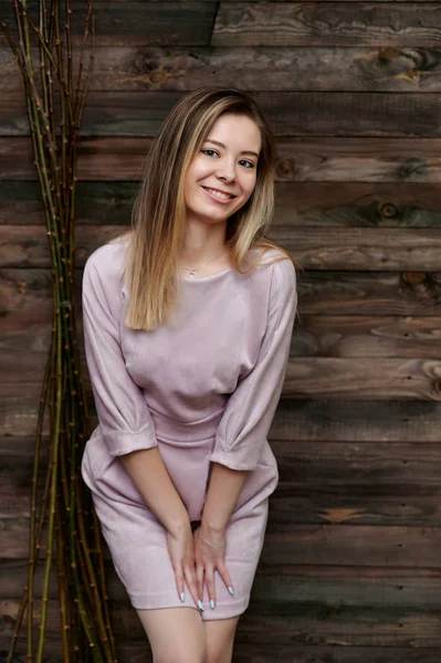 Concepto de estilo loft. Retrato de una hermosa chica sonriente en un bonito vestido rosa sobre un fondo de interior en una habitación de madera. Muestra felicidad, sonrisa, amabilidad. De pie frente a la cámara . — Foto de Stock
