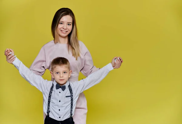 Portrait of a happy family: mom and a cute boy of 10 years of schoolboy on a yellow background in trousers and a shirt. Standing right in front of the camera, showing emotions, smile — Stock Photo, Image