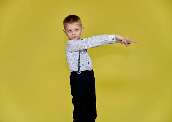 Portret uroczego chłopca 10-letniego ucznia na żółtym tle w spodniach i koszuli. Stojąc tuż przed kamerą, pokazuje emocje, mówi w różnych pozach. — Zdjęcie stockowe