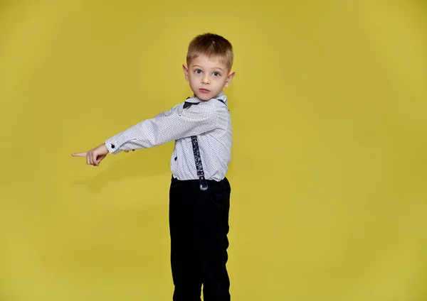 Portret van een leuke jongen van 10 jaar op een gele achtergrond in een broek en een shirt. Staande recht voor de camera, Toont emoties, praat in verschillende houdingen. — Stockfoto