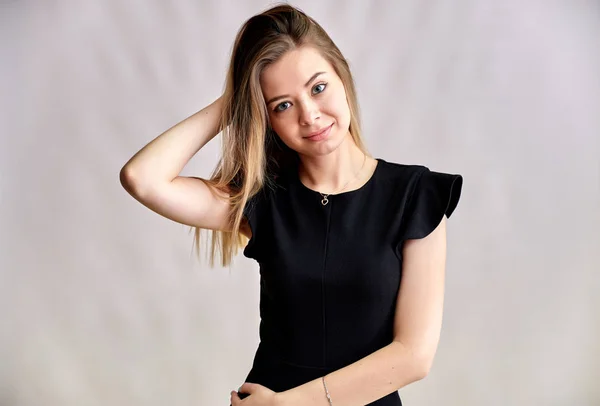 Close-up portrait of a pretty young smiling woman on a gray background in a black dress with long straight hair. Standing right in front of the camera, Shows emotions, talks in different poses. — Stock Photo, Image