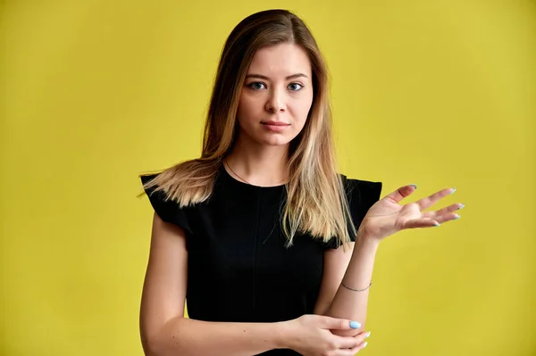 Close-up portrait of a pretty young smiling woman on a yellow background in a black dress with long straight hair. Standing right in front of the camera, Shows emotions, talks in different poses. — Stock Photo, Image
