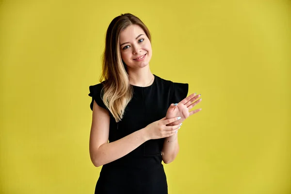 Retrato de una bonita joven sonriente sobre un fondo amarillo en un vestido negro con pelo largo y liso. De pie frente a la cámara, muestra emociones, habla en diferentes poses . — Foto de Stock
