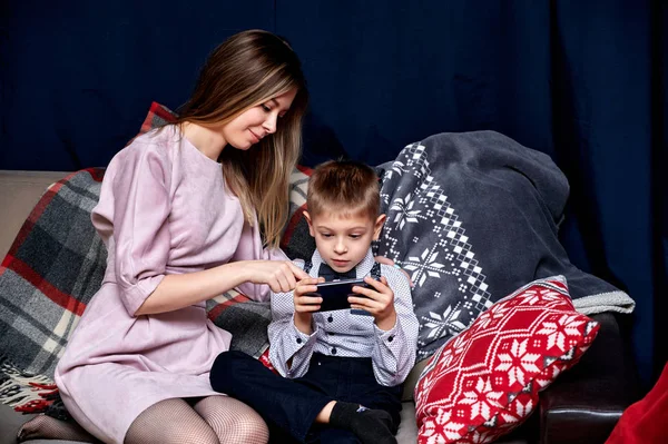 Portrait of a happy family: mom and a cute boy of 10 years of schoolboy with a smartphone at home on the sofa. Sitting right in front of the camera, showing emotions, smile — Stock Photo, Image