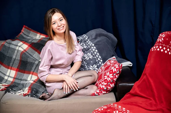 Retrato de una hermosa chica con el pelo largo en un vestido rosa sentado en casa en un sofá en un estilo loft. Sentada frente a la cámara, mostrando emociones felices, sonriendo — Foto de Stock