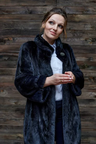 木製の背景に毛皮のコートで40年の大人のきれいな女性の肖像画。ビジネスコンセプト。深刻な気分でカメラの前に立って. — ストック写真
