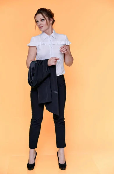 Business concept. Full-length portrait of an adult pretty woman of 40 years old with good makeup in a business suit on a yellow background. Standing right in front of the camera with a smile. — ストック写真