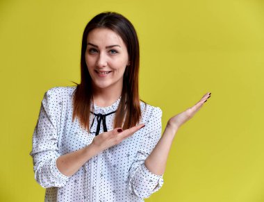 Bir ofis çalışanı, öğretmen, yönetici konsepti. Beyaz iş gömleği giymiş güzel esmer bir kızın portresi. Gülümsüyor, sarı arka planda kameraya konuşuyor..