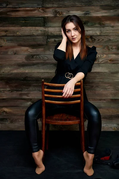 The concept of a glamorous portrait. Portrait of a pretty brunette girl in a black fashion suit on a stylish background in the original interior. Sits on a chair in various poses. — Stock Photo, Image