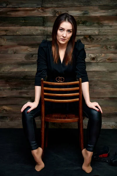 Koncept okouzlujícího portrétu. Portrét hezké brunetky v černém módním obleku na stylovém pozadí v původním interiéru. Sedí na židli v různých pózách. — Stock fotografie