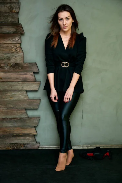 The concept of a glamorous portrait. Portrait of a pretty brunette girl in a black fashion suit on a stylish background in the original interior. Stands in front of the camera in various poses.