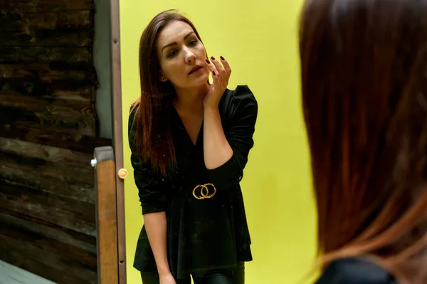 आरशासमोर ग्लॅमरस पोर्ट्रेटची संकल्पना. एक काळा फॅशन सूट मध्ये एक सुंदर श्यामला मुलगी पोर्ट्रेट मूळ आरसा समोर मेकअप तपासणी . — स्टॉक फोटो, इमेज
