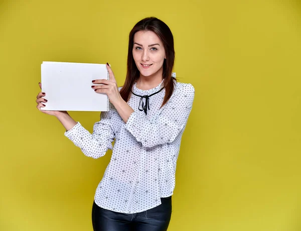 Il concetto di impiegato, insegnante, manager. Ritratto di una bella ragazza bruna in una camicetta bianca sorridente, che parla con la macchina fotografica su uno sfondo giallo con una cartella in mano . — Foto Stock