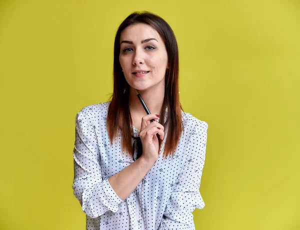The concept of an office worker, teacher, manager. Portrait of a pretty brunette girl in a white business blouse smiling, talking to the camera on a yellow background. — Stock Photo, Image