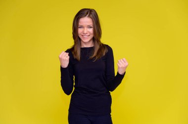 Olumlu duyguları olan gülümseyen tatlı bir kız konsepti. Siyah tişörtlü genç bir kadının portresi sarı arka planda uzun saçlı farklı pozlarda duruyor. Elleri göster, konuş..