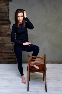 Çekici bir esmerin stüdyosundaki şık bir koltuğun içinde dikey bir fotoğraf. Uzun saçlı siyah tişörtlü bir kız alternatif moda arka planında duruyor..