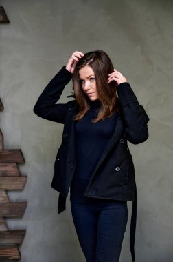 Çekici bir esmerin stüdyosundaki şık bir iç mekandaki kıyafetlerin dikey fotoğrafı. Kız farklı pozlarda duruyor. Uzun saçları var. Renkli, orijinal bir arka planı var..