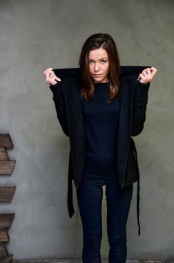 Çekici bir esmerin stüdyosundaki şık bir iç mekandaki kıyafetlerin dikey fotoğrafı. Kız farklı pozlarda duruyor. Uzun saçları var. Renkli, orijinal bir arka planı var..