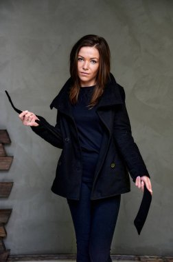 Çekici bir esmerin stüdyosundaki şık bir iç mekandaki kıyafetlerin dikey fotoğrafı. Kız farklı pozlarda duruyor. Uzun saçları var. Renkli, orijinal bir arka planı var..