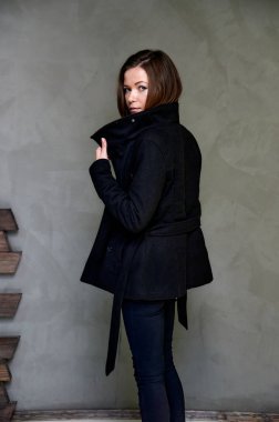 Çekici bir esmerin stüdyosundaki şık bir iç mekandaki kıyafetlerin dikey fotoğrafı. Kız farklı pozlarda duruyor. Uzun saçları var. Renkli, orijinal bir arka planı var..