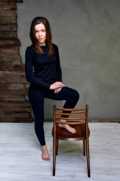 Photo verticale avec une chaise dans un intérieur élégant dans le studio d'une jolie brune glamour. fille se tient dans un T-shirt noir avec des cheveux longs sur un fond original à la mode alternative de couleur . — Photo