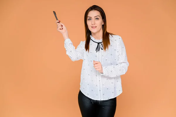 Concepto de secretario. Retrato de una mujer bonita, gerente en una blusa blanca con el pelo suave y oscuro. Él está de pie justo delante de la cámara, sonriendo, mostrando emociones sobre un fondo naranja . — Foto de Stock