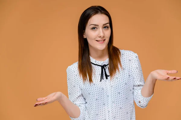 Concepto de secretario. Retrato de una mujer bonita, gerente en una blusa blanca con el pelo suave y oscuro. Él está de pie justo delante de la cámara, sonriendo, mostrando emociones sobre un fondo naranja . — Foto de Stock