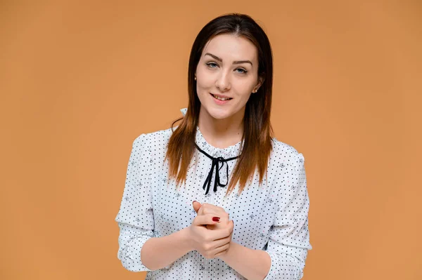 Concepto de secretario. Retrato de una mujer bonita, gerente en una blusa blanca con el pelo suave y oscuro. Él está de pie justo delante de la cámara, sonriendo, mostrando emociones sobre un fondo naranja . — Foto de Stock