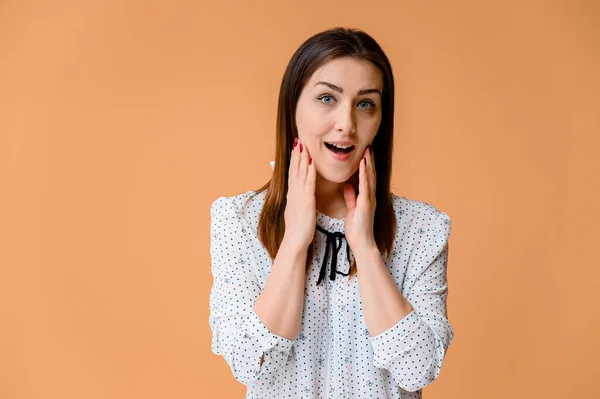 Concepto de secretario. Retrato de una mujer bonita, gerente en una blusa blanca con el pelo suave y oscuro. Él está de pie justo delante de la cámara, sonriendo, mostrando emociones sobre un fondo naranja . — Foto de Stock