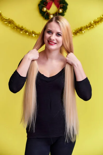 Concept d'une jeune femme blonde au décor de Nouvel An. Portrait d'une jolie fille dans un T-shirt noir avec de longs beaux cheveux et un excellent maquillage. Souriant, montrant des émotions sur un fond jaune . — Photo