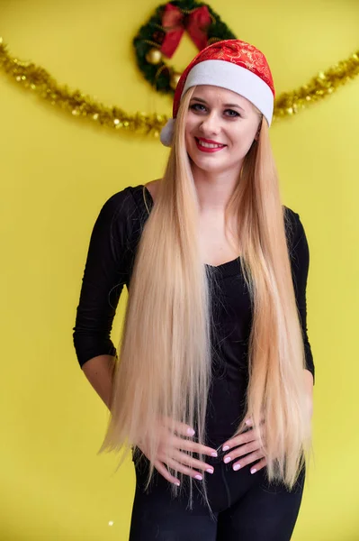 Concept d'une jeune femme blonde au décor de Nouvel An. Portrait d'une jolie fille dans un T-shirt noir avec de longs beaux cheveux et un excellent maquillage. Souriant, montrant des émotions sur un fond jaune . — Photo