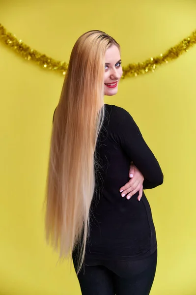 クリスマスの装飾、リアビューを持つ若いブロンドの女性の概念。長い美しい髪と素晴らしいメイクの黒いTシャツのかわいい女の子の肖像画。黄色の背景で微笑む. — ストック写真